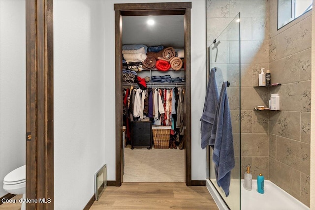 bathroom with wood-type flooring, toilet, and a shower with door