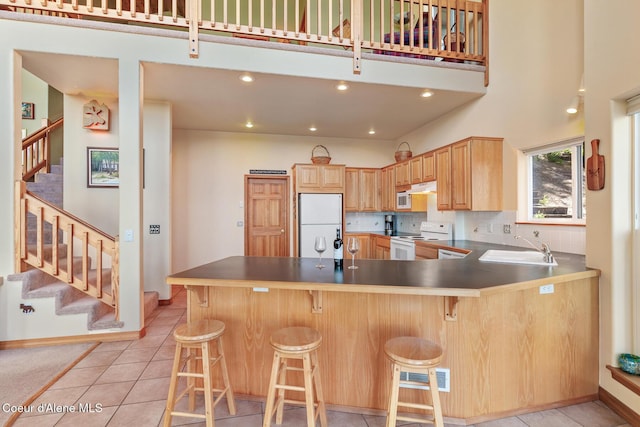 kitchen with sink, a kitchen bar, light tile patterned floors, kitchen peninsula, and white appliances