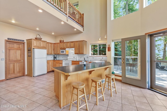 kitchen with a towering ceiling, white appliances, a kitchen breakfast bar, and light tile patterned floors