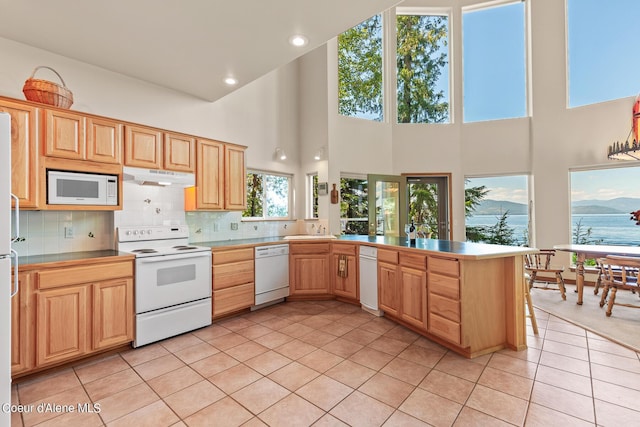 kitchen featuring a towering ceiling, sink, light tile patterned floors, kitchen peninsula, and white appliances