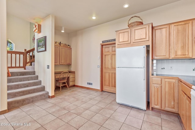 kitchen with light tile patterned floors, white refrigerator, tasteful backsplash, built in desk, and light brown cabinetry