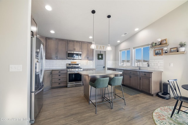 kitchen featuring pendant lighting, lofted ceiling, appliances with stainless steel finishes, a kitchen breakfast bar, and a center island