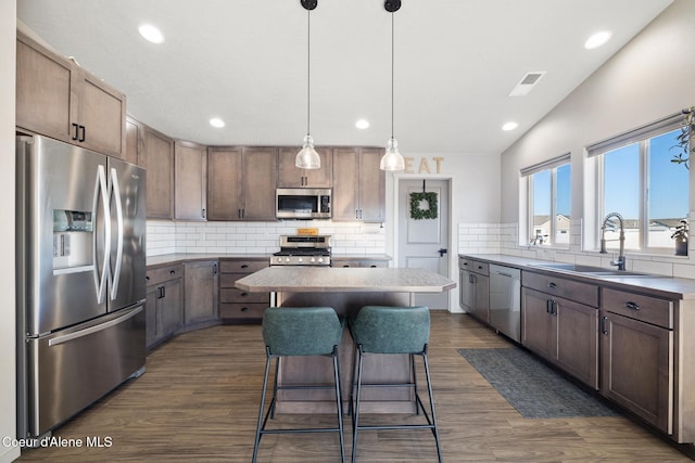 kitchen featuring sink, dark wood-type flooring, stainless steel appliances, a kitchen island, and decorative light fixtures