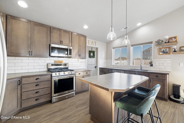 kitchen featuring lofted ceiling, a breakfast bar area, appliances with stainless steel finishes, a kitchen island, and light hardwood / wood-style floors