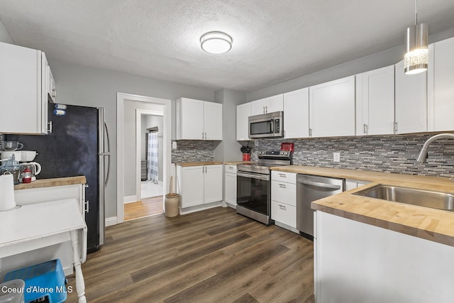 kitchen featuring wood counters, white cabinetry, sink, hanging light fixtures, and stainless steel appliances