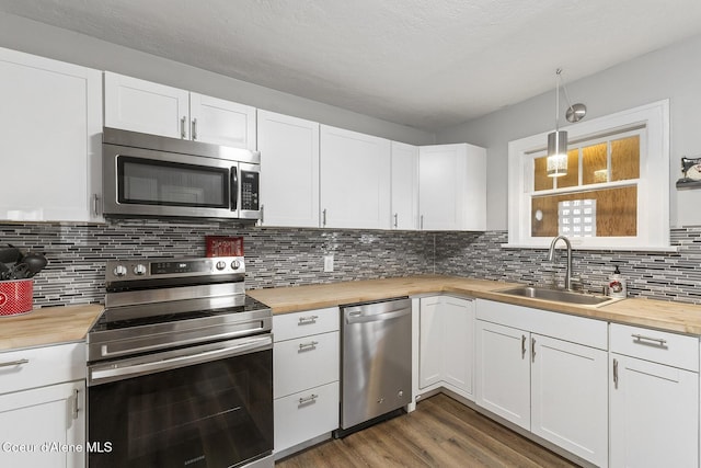 kitchen featuring sink, butcher block countertops, white cabinetry, hanging light fixtures, and stainless steel appliances