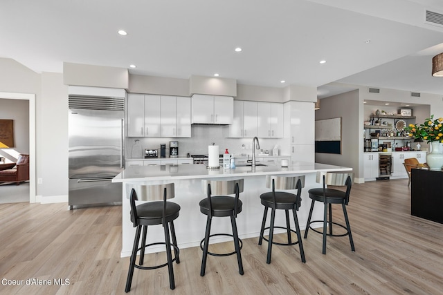 kitchen featuring a breakfast bar, white cabinetry, built in refrigerator, a large island with sink, and light hardwood / wood-style flooring