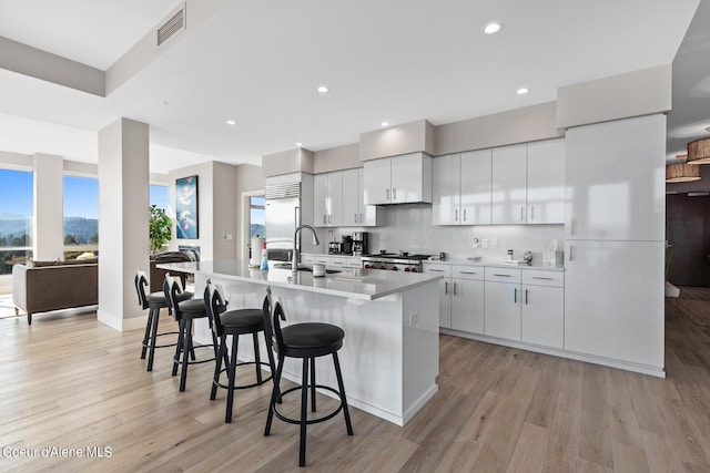 kitchen with an island with sink, stainless steel built in refrigerator, sink, white cabinets, and decorative backsplash