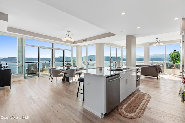 kitchen featuring a water and mountain view, a center island with sink, light hardwood / wood-style flooring, dishwasher, and white cabinets