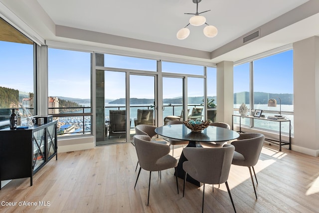 dining space with a notable chandelier, a wealth of natural light, a water and mountain view, and light hardwood / wood-style floors