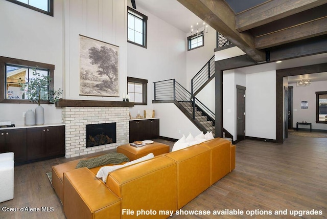 living room with dark wood-type flooring, beam ceiling, a high ceiling, a fireplace, and a chandelier