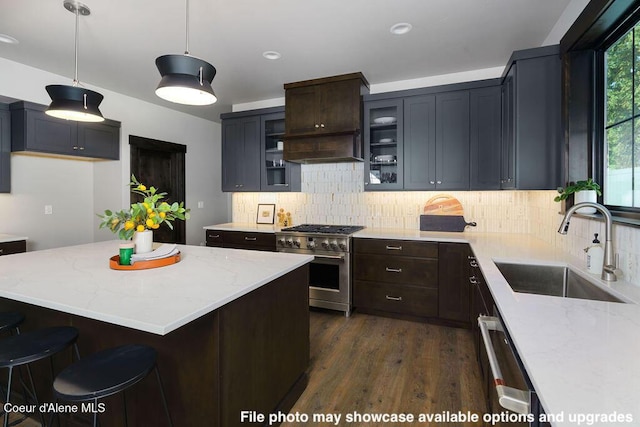 kitchen with sink, decorative backsplash, hanging light fixtures, high end stainless steel range, and light stone counters