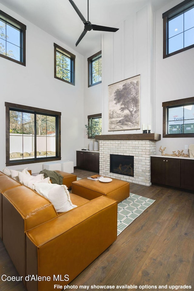 living room with dark wood-type flooring, ceiling fan, a fireplace, and a high ceiling