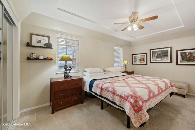 bedroom with ceiling fan, a tray ceiling, and light carpet