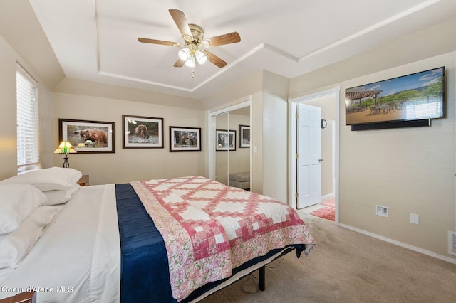 carpeted bedroom with a raised ceiling, a closet, and ceiling fan