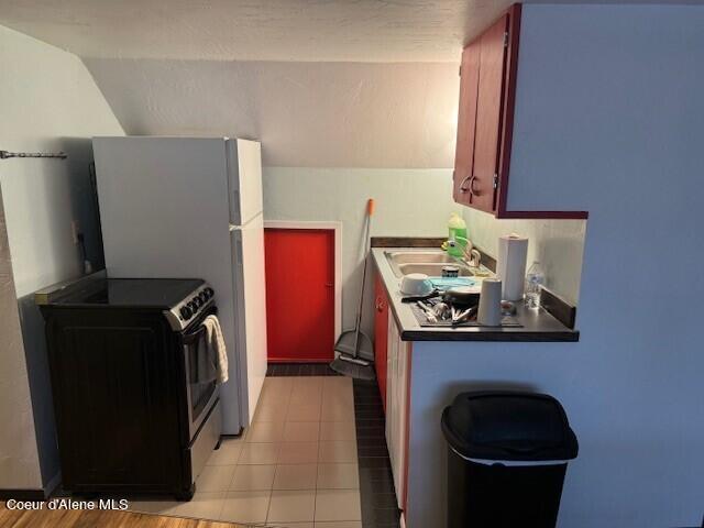 kitchen with vaulted ceiling, sink, light tile patterned floors, and electric range oven
