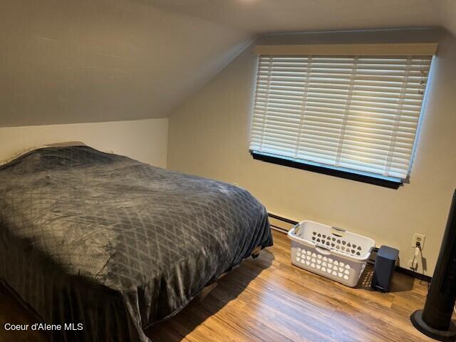 bedroom featuring lofted ceiling, a baseboard radiator, and light wood-type flooring