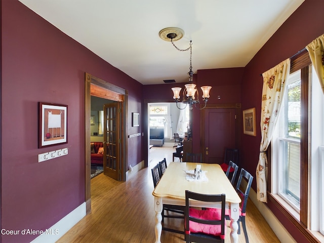 dining area with wood-type flooring, plenty of natural light, and an inviting chandelier