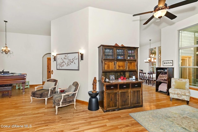 living room with a high ceiling, ceiling fan with notable chandelier, and light wood-type flooring