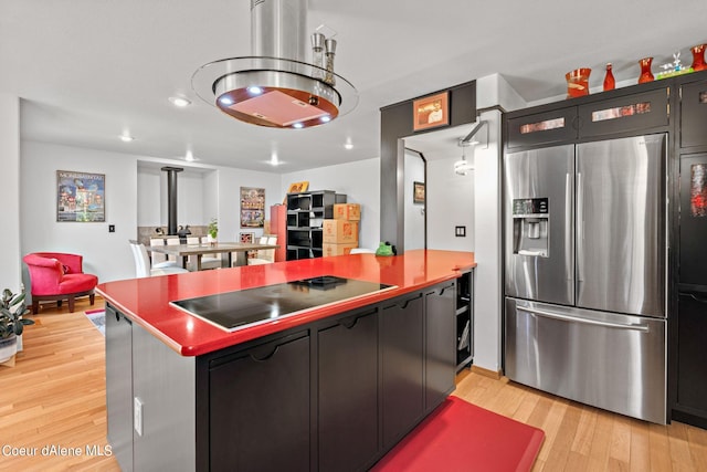 kitchen featuring light hardwood / wood-style flooring, black electric stovetop, stainless steel fridge with ice dispenser, kitchen peninsula, and a wood stove