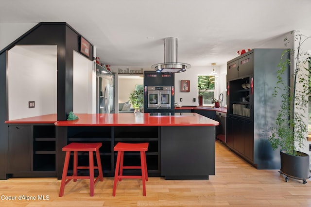 kitchen with appliances with stainless steel finishes, a kitchen bar, sink, and light wood-type flooring