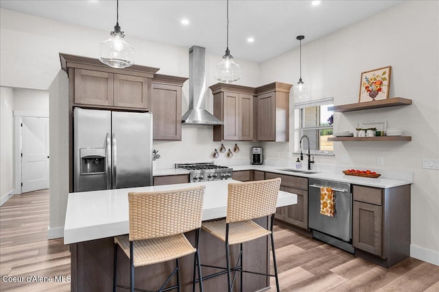 kitchen featuring sink, hanging light fixtures, light wood-type flooring, appliances with stainless steel finishes, and wall chimney range hood