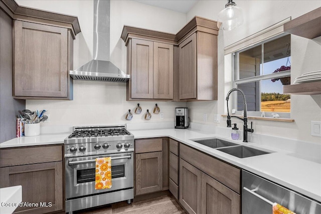 kitchen featuring stainless steel appliances, sink, wall chimney range hood, and decorative light fixtures