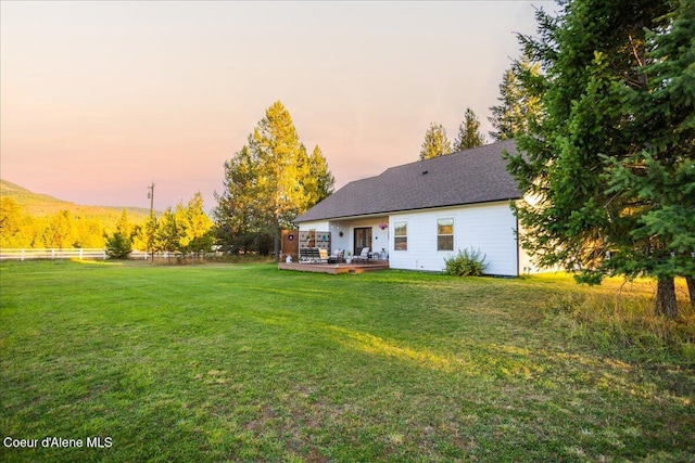 back house at dusk featuring a wooden deck and a yard