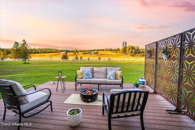 deck at dusk with a yard, an outdoor living space with a fire pit, and a rural view