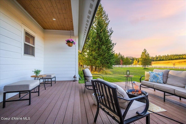 deck at dusk with a lawn and an outdoor living space with a fire pit