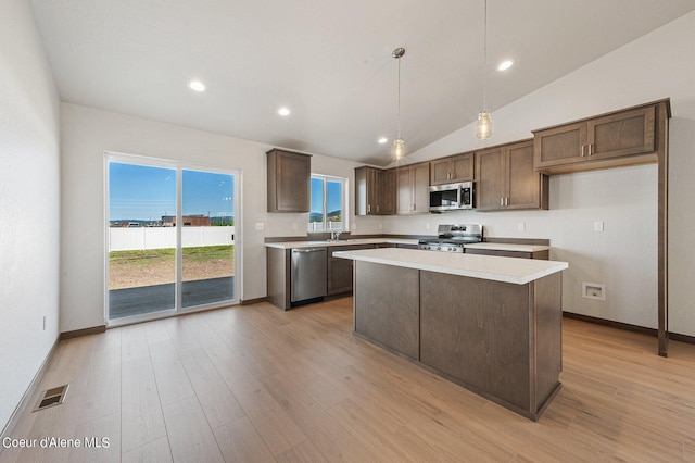 kitchen with pendant lighting, lofted ceiling, appliances with stainless steel finishes, light hardwood / wood-style floors, and a kitchen island