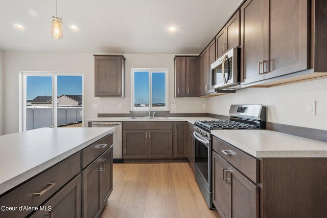 kitchen featuring dark brown cabinetry, sink, hanging light fixtures, light hardwood / wood-style flooring, and appliances with stainless steel finishes