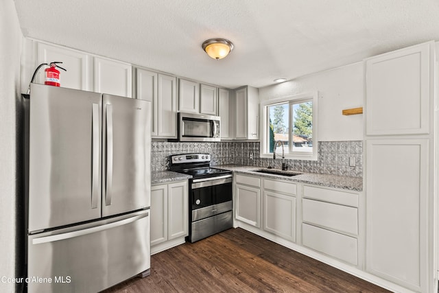 kitchen featuring sink, dark wood-type flooring, stainless steel appliances, light stone counters, and decorative backsplash