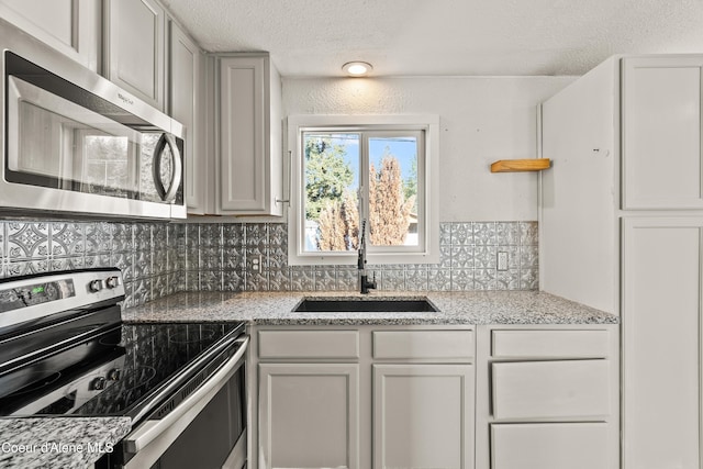 kitchen featuring sink, backsplash, stainless steel appliances, light stone countertops, and a textured ceiling