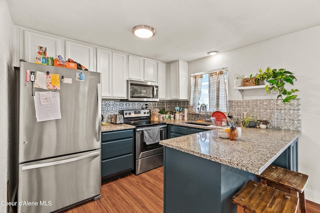 kitchen with sink, a breakfast bar area, appliances with stainless steel finishes, kitchen peninsula, and white cabinets