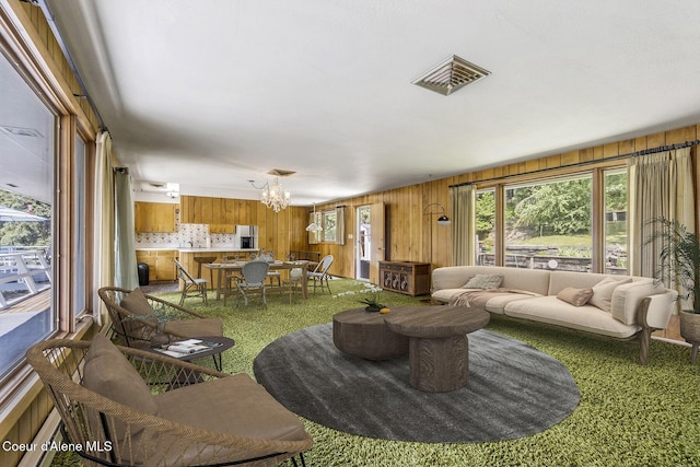 carpeted living room featuring a notable chandelier and wooden walls