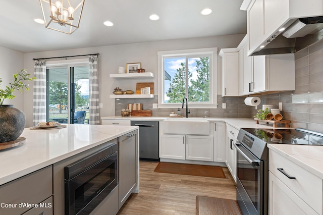 kitchen featuring decorative backsplash, stainless steel appliances, wall chimney range hood, a sink, and recessed lighting