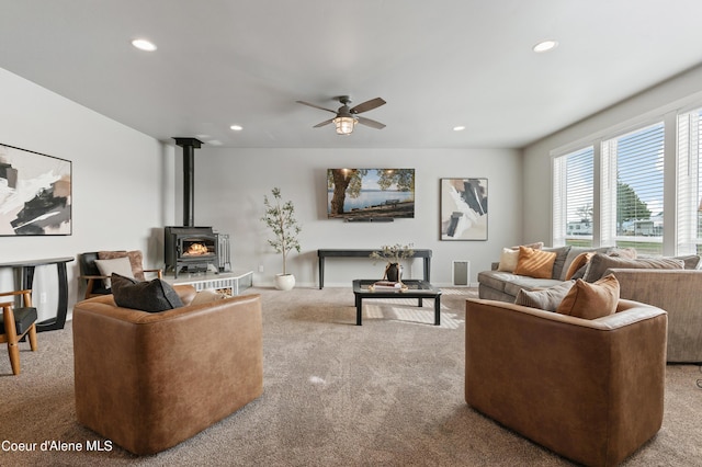 carpeted living room with ceiling fan and a wood stove