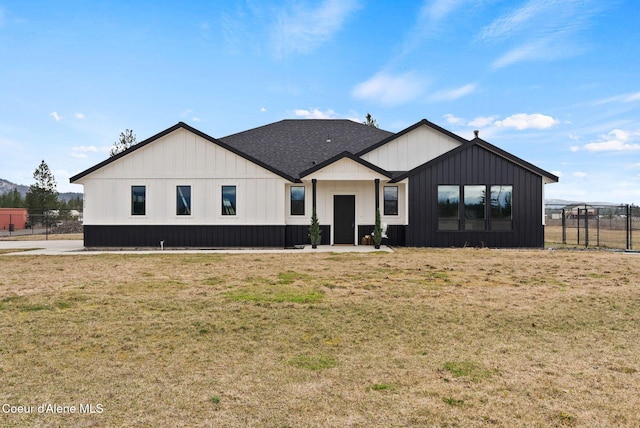 back of property with roof with shingles, fence, board and batten siding, and a yard