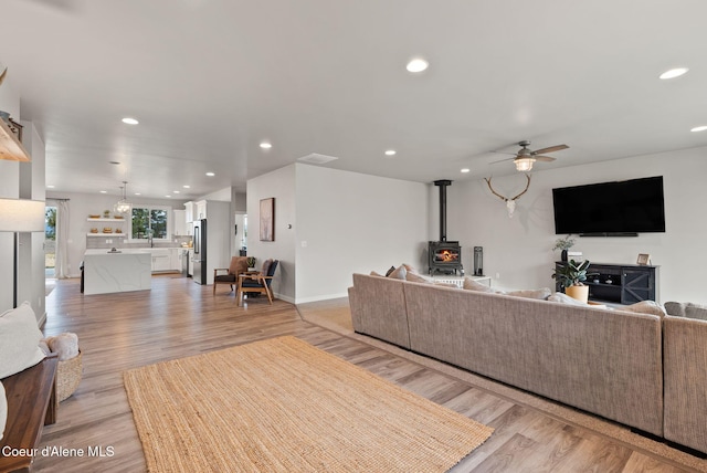 living area featuring recessed lighting, light wood-style floors, ceiling fan, and a wood stove