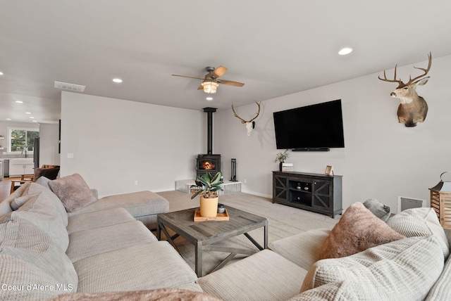 living area with a wood stove, light colored carpet, visible vents, ceiling fan, and recessed lighting