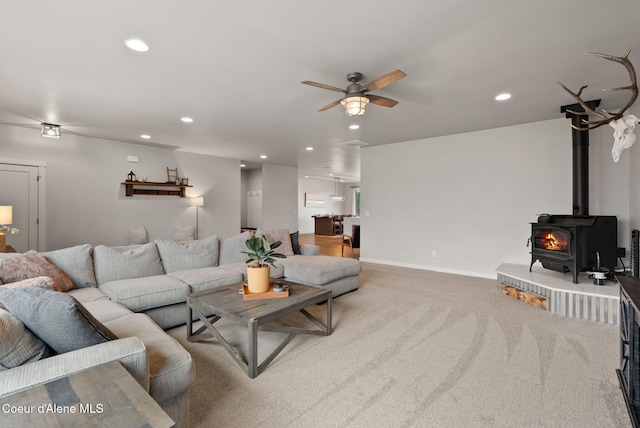 carpeted living area with baseboards, a wood stove, recessed lighting, and a ceiling fan