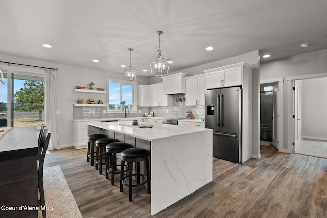 kitchen with wood finished floors, a kitchen island, appliances with stainless steel finishes, white cabinetry, and backsplash