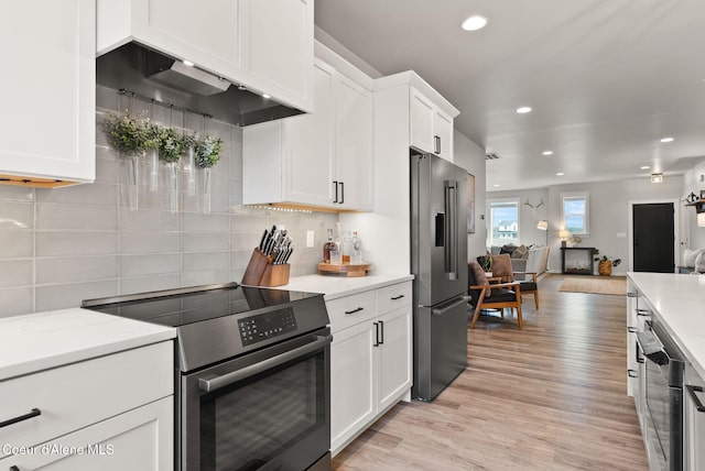 kitchen featuring open floor plan, white cabinetry, decorative backsplash, light wood-style flooring, and appliances with stainless steel finishes