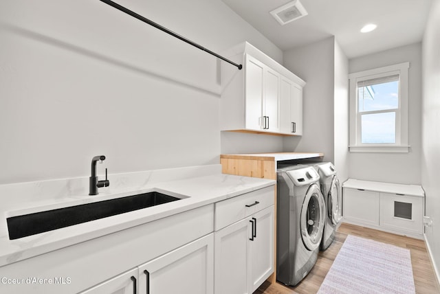 washroom with a sink, light wood finished floors, washing machine and clothes dryer, visible vents, and cabinet space