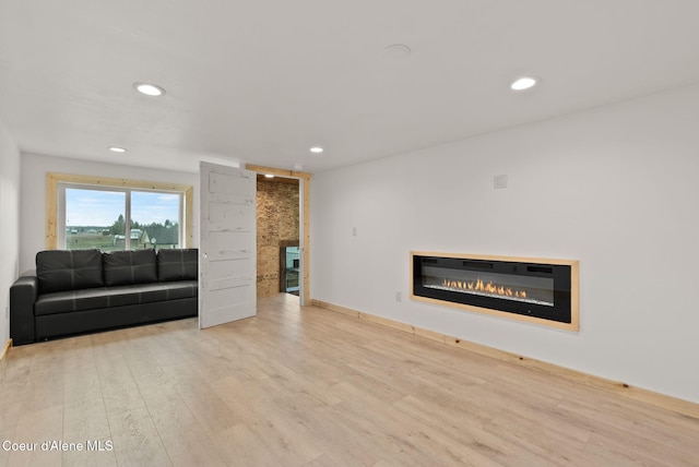 living room featuring recessed lighting, a glass covered fireplace, and wood finished floors
