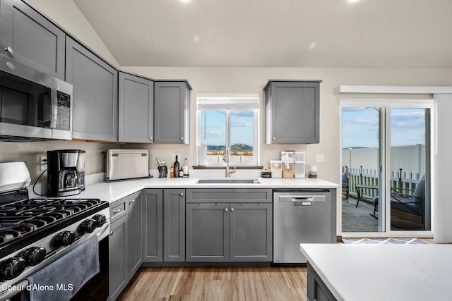 kitchen with gray cabinets, appliances with stainless steel finishes, lofted ceiling, sink, and light hardwood / wood-style floors