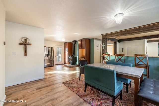 dining space featuring beam ceiling, a wood stove, and light hardwood / wood-style floors