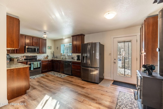 kitchen with light stone counters, stainless steel appliances, decorative backsplash, and light wood-type flooring