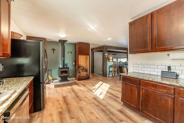 kitchen with a wood stove, dishwashing machine, stainless steel fridge, light stone countertops, and light wood-type flooring